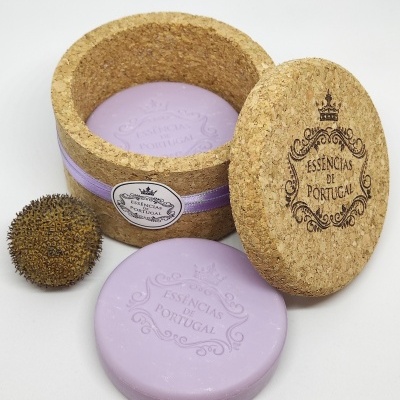 Sabonete lilás redondo dentro de caixa de cortiça redonda, com tampa gravada e fruto seco ao lado.