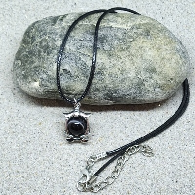 Colar preto com pendente prateado e pedra preta sobre pedra e areia