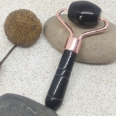 Rolo facial preto com estrutura metálica cor-de-rosa sobre pedras e flor seca