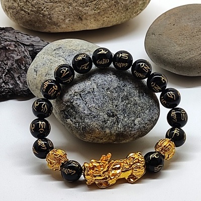 Pulseira preta com inscrições douradas e peça central dourada em forma de dragão sobre pedras lisas
