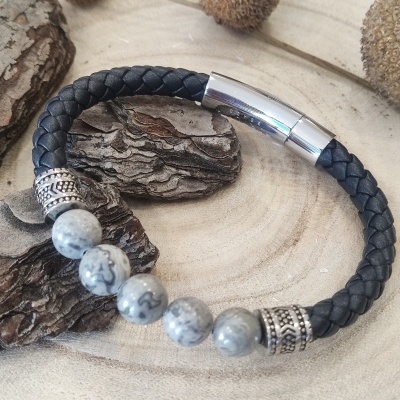 Pulseira masculina preta com contas de pedra cinza e detalhes metálicos sobre madeira natural clara.