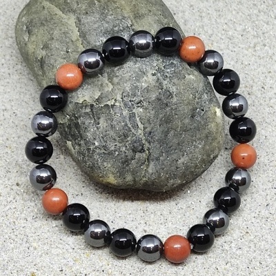 Pulseira com contas pretas, cinza metálico e terracota sobre pedra cinza