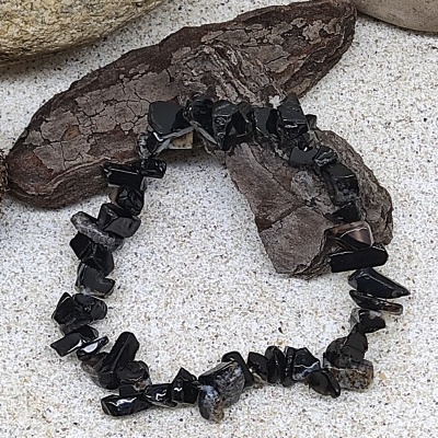 Pulseira de pedras pretas brilhantes sobre superfície clara com pedras ao redor