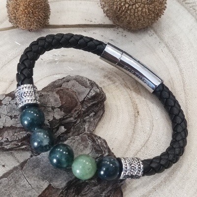 Pulseira preta trançada com contas verdes e fecho metálico sobre madeira clara