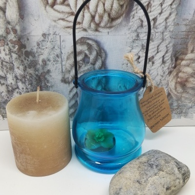 Vela castanha, vaso azul de vidro com planta verde e pedra cinzenta sobre superfície branca