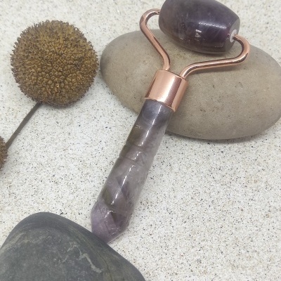 Rolo facial de pedra ametista com suporte de metal cor cobre sobre pedras e planta seca
