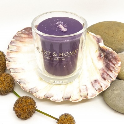 Vela roxa em copo de vidro sobre concha grande com flores secas e pedras