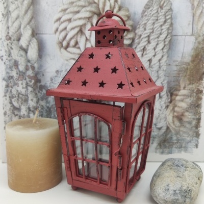Lanterna decorativa vermelha metálica com estrelas, vela bege e pedra cinzenta em fundo com cordas