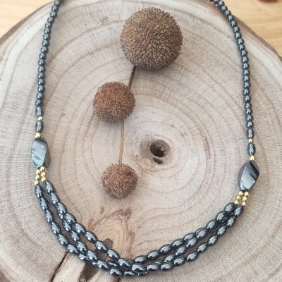 Colar com contas cinza e douradas sobre base de madeira redonda com sementes secas