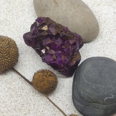 Cristal ametista roxo com pedras lisas e flores secas em areia clara