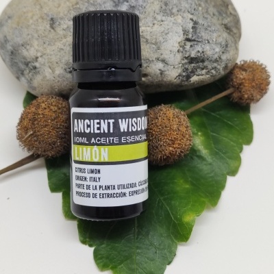 Frasco de óleo essencial de limão junto a uma pedra e folhas verdes