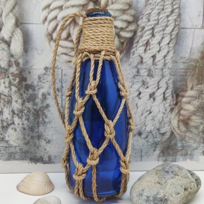 Garrafa azul de vidro com suporte de corda em padrão de rede, moluscos e pedra ao lado