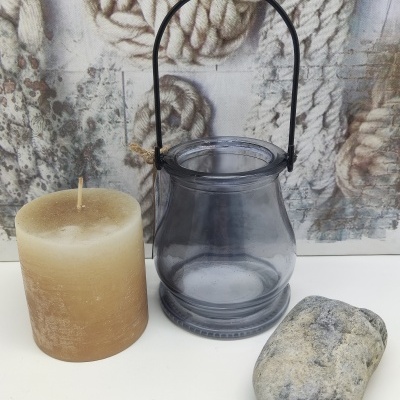 Vela castanha, suporte de vidro cinzento com alça preta e pedra cinzenta sobre superfície branca