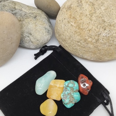 Pedras semipreciosas coloridas sobre saco preto de veludo com pedras naturais maiores ao redor