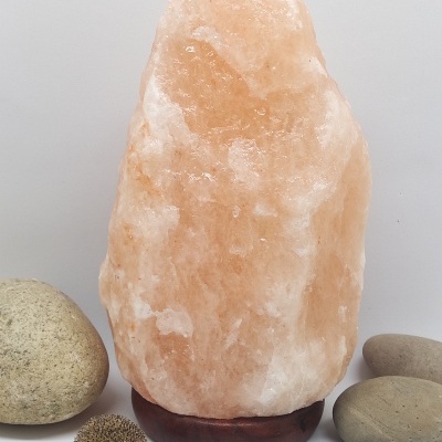 Lâmpada de sal rosa com base de madeira escura e pedras ao redor