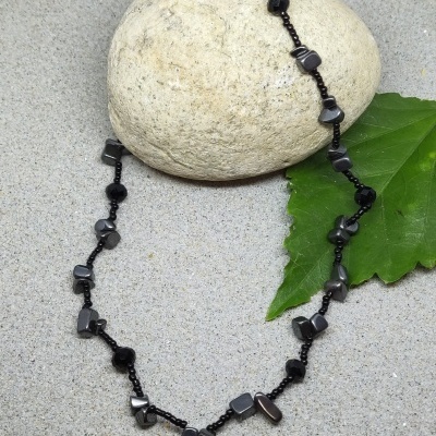 Colar com pedras pretas e cinzentas sobre pedra clara e folha verde
