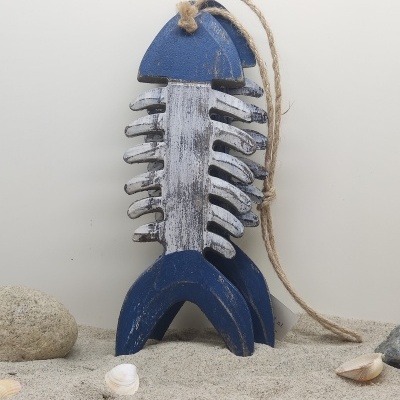 Decoração de madeira em forma de esqueleto de peixe azul e branco pendurada por cordão de juta sobre areia com conchas e pedras