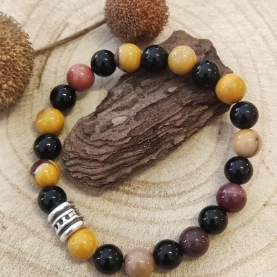 Pulseira de contas coloridas com peça metálica sobre madeira seca e elementos naturais