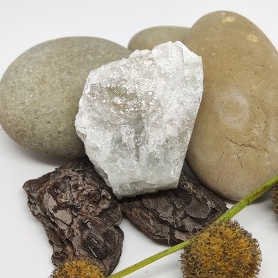 Pedras lisas, pedra branca cristalina, casca marrom e flores secas amarelas sobre fundo branco.