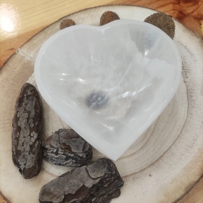 Prato de madeira claro com cascas de árvore e um recipiente translúcido branco em forma de coração no centro