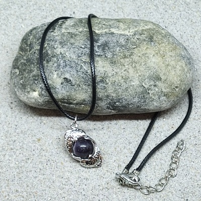 Colar com pendente metálico prateado e pedra escura sobre pedra cinzenta