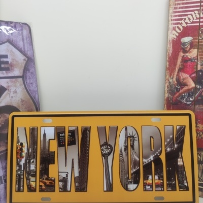Placa decorativa amarela com a palavra NEW YORK preenchida com imagens da cidade de Nova Iorque.