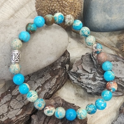 Pulseira elástica com contas azuis e bege sobre madeira e pedras