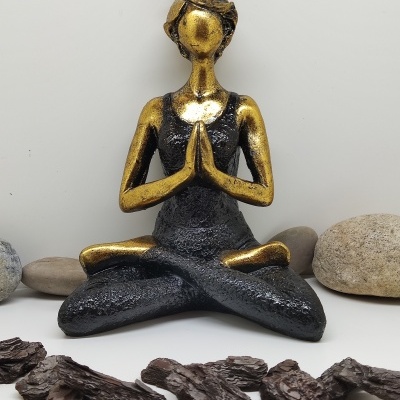 Estátua decorativa de mulher em meditação com pedras e madeira ao redor