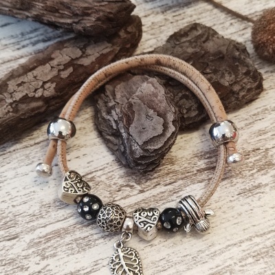 Pulseira com contas em metal prateado e cordão castanho claro sobre madeira