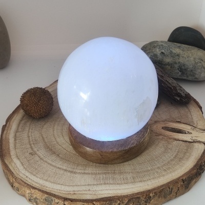 Esfera de cristal branca em base de madeira sobre tronco com pedras ao fundo