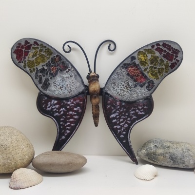 Escultura decorativa de borboleta com asas em mosaico colorido sobre superfície branca com pedras e conchas