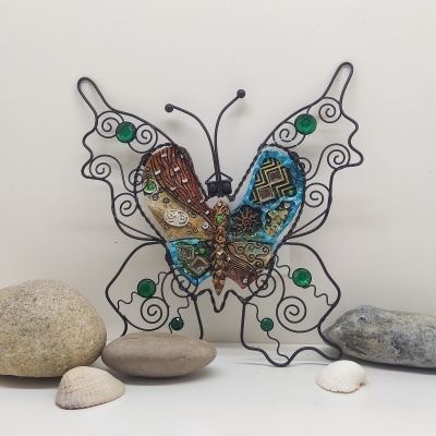 Escultura metálica de borboleta com pedras verdes e padrões multicoloridos