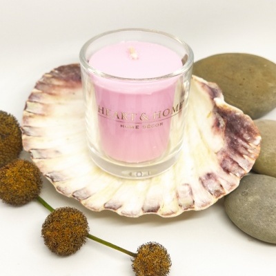 Vela rosa em copo de vidro dentro de concha com pedras e flores secas