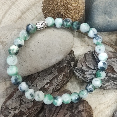 Pulseira de contas verdes e brancas com entremeio metálico sobre pedras e madeira
