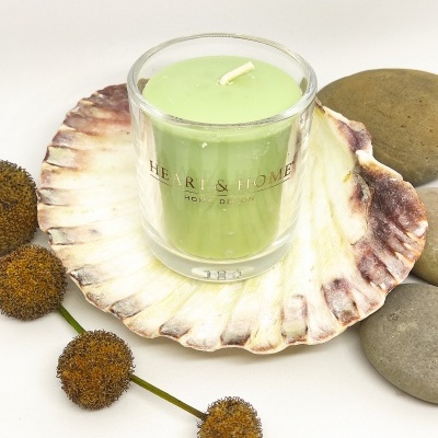 Vela verde em copo de vidro numa concha decorativa com pedras e flores secas