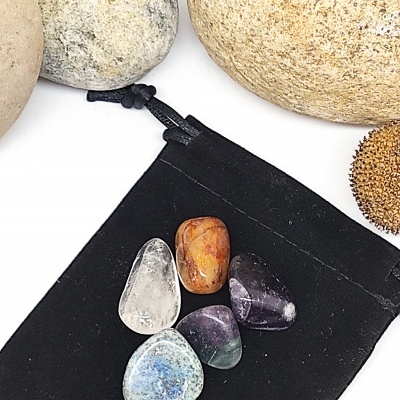 Cinco pedras polidas coloridas sobre saco preto com pedras grandes ao fundo