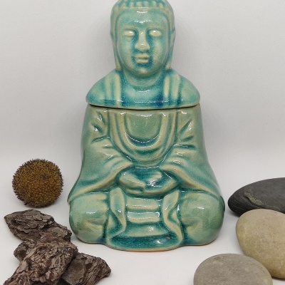 Frasco cerâmico azul-esverdeado em forma de Buda com pedras naturais em fundo branco.