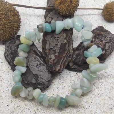 Bracelete de pedras azul-esverdeadas sobre casca de árvore com fundo de areia e elementos naturais secos