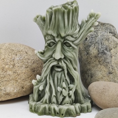 Vela verde esculpida em forma de rosto de homem árvore com pedras ao redor