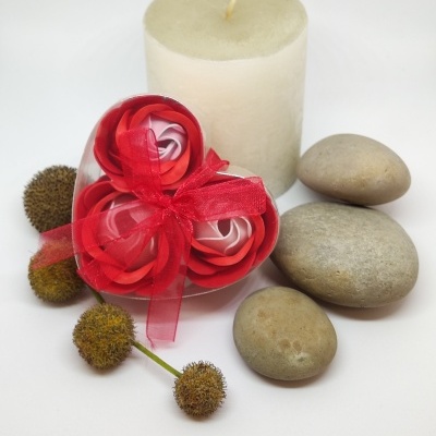 Vela branca com flores artificiais em embalagem de coração, pedras lisas e flores secas num fundo branco