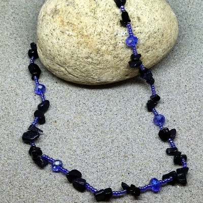 Colar azul com pedras pretas sobre areia e pedra clara