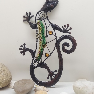 Escultura decorativa de lagarto em metal com vidro colorido rodeado por pedras e conchas