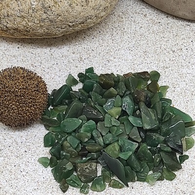 Pedras verdes irregulares com pedras grandes e esfera marrom numa superfície clara.