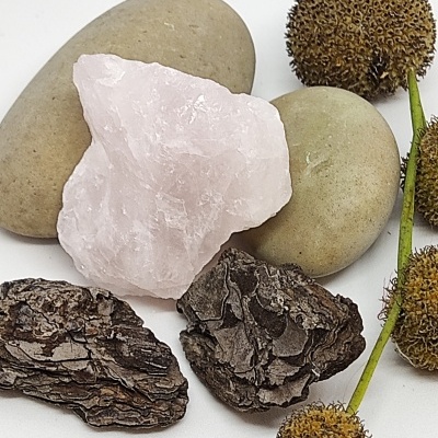 Pedras decorativas incluindo quartzo rosa, pedras lisas cinza, casca de árvore castanha e ramos com bolotas secas