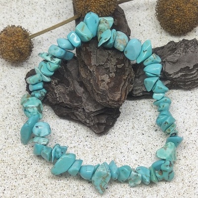 Pulseira de pedras azuis irregulares com manchas castanhas em fundo de areia e cascas de árvore