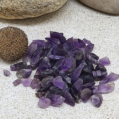 Pequenas pedras roxas sobre superfície clara, próximas a pedras arredondadas maiores e uma esfera castanha.