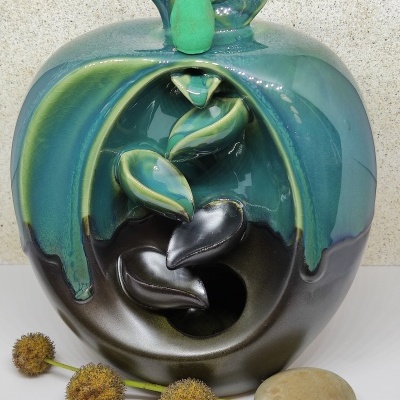 Escultura cerâmica maçã azul e preta com folhas verdes e objetos decorativos