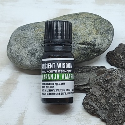 Frasco pequeno de óleo essencial com pedra e casca em superfície de madeira clara