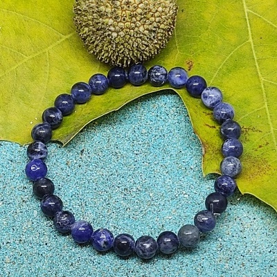 Pulseira de contas de pedra azul com uma semente e folha verde sobre superfície azul