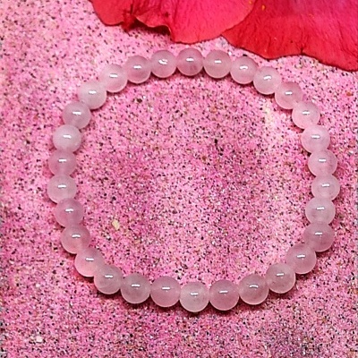 Pulseira de contas de quartzo rosa sobre fundo rosa com flor vermelha